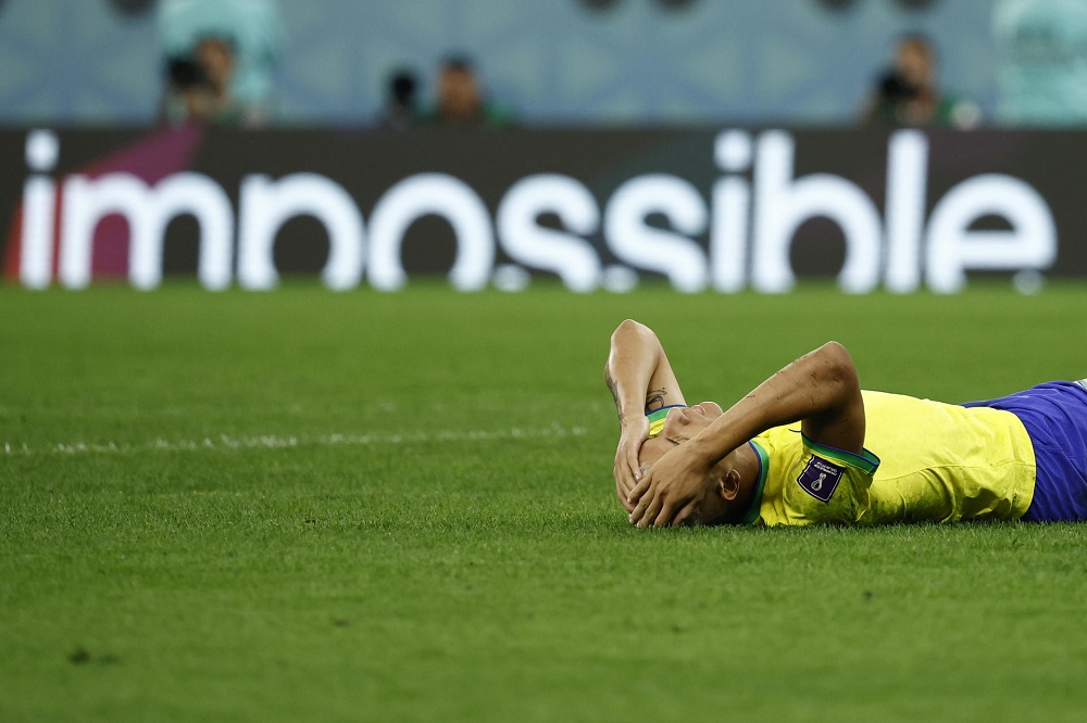 Richarlison caído no gramado com as mãos na cabeça