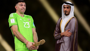 Martínez coloca seu prêmio de melhor goleiro perto do pênis e faz careta, recebendo olhares de um homem com trajes árabes