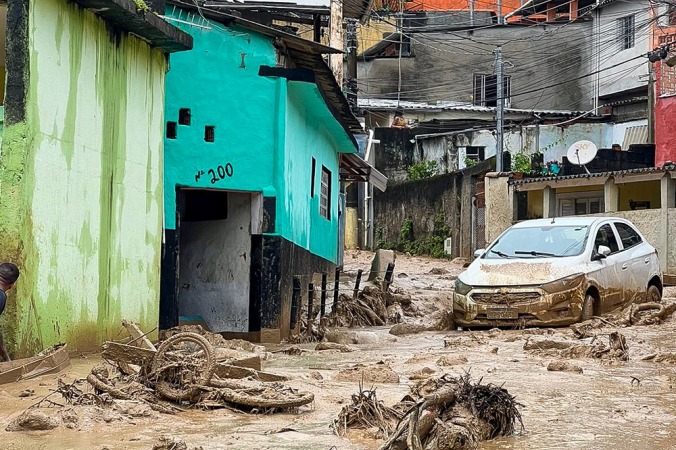 Rua em São Sebstião coberta de água barrenta, com carro e bicicleta destruídos