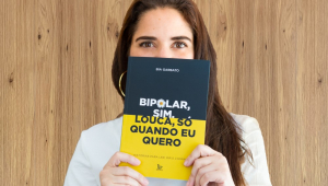 Foto da colunista Bia Garbato segurando um livro que cobre metade do seu rosto