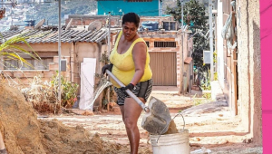 Mulher com pá jogando terra no balde em casa na favela
