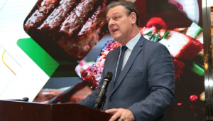 Carlos Fávaro, ministro da Agricultura, participa de seminário de traje social, com um painel mostrando carne bovina atrás dele