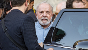 Lula perto da porta de um carro preto, cercado por seguranças