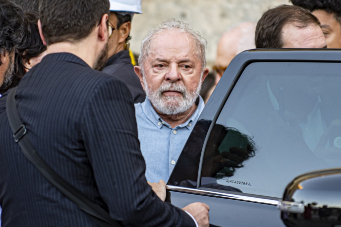 Lula perto da porta de um carro preto, cercado por seguranças