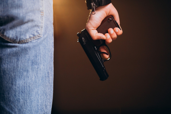 Na imagem, aparece um hpmem de calça jeans, segurando uma arma