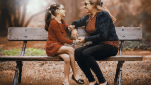 Mulher e filha sentadas num banco olham uma para outra