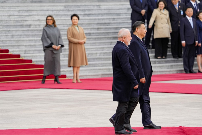 Lula caminha ao lado de i Jinping, e ao fundo aparecem Janja e a primeira-dama chinesa