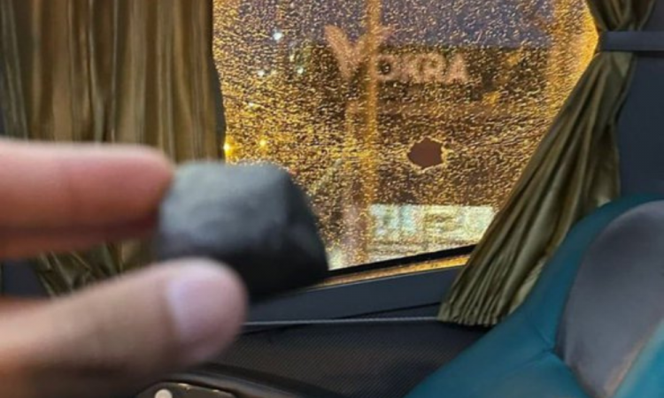 Jogador do Tigre segura uma pedra e mostra o vidro da janela do ônibus quebrado