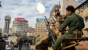 Um combatente rebelde sírio dispara tiros enquanto pessoas comemoram perto da Torre do Relógio, na cidade central de Homs