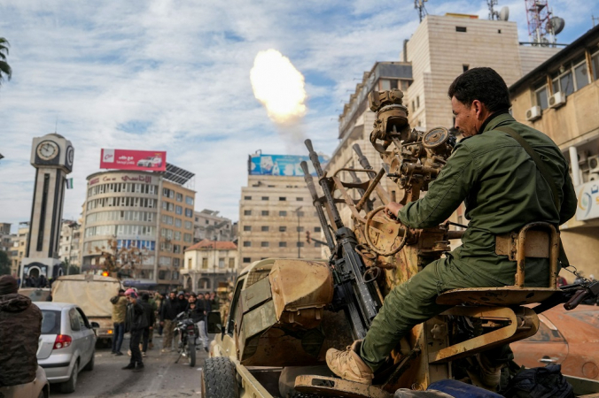 Um combatente rebelde sírio dispara tiros enquanto pessoas comemoram perto da Torre do Relógio, na cidade central de Homs