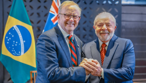 Com as bandeiras de Brasil e Austrália atrás, Anthony Albanese e Lula apertam as mãos e sorriem