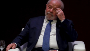 Lula com a mão no olho e olhar pensativo, sentado em cadeira, em evento na Fiesp
