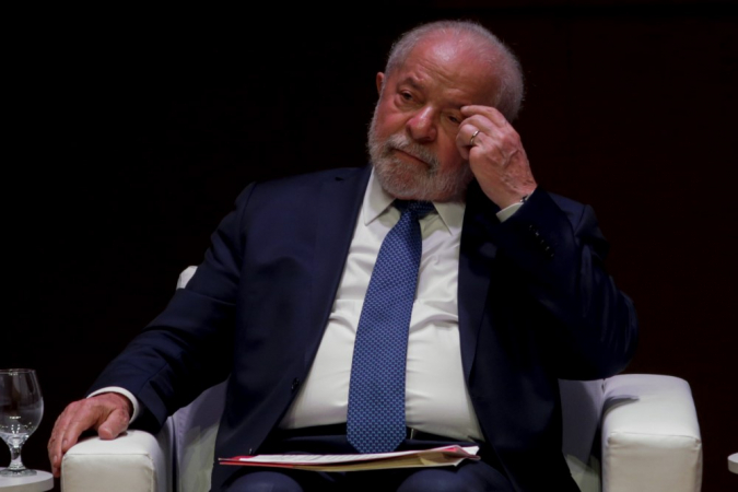 Lula com a mão no olho e olhar pensativo, sentado em cadeira, em evento na Fiesp