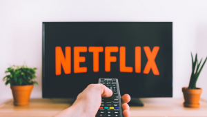 Braço com controle apponta para TV comlogo do Netflix