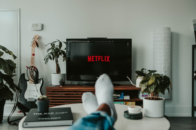 Homem com os pés na mesa assiste à TV logada no Netflix