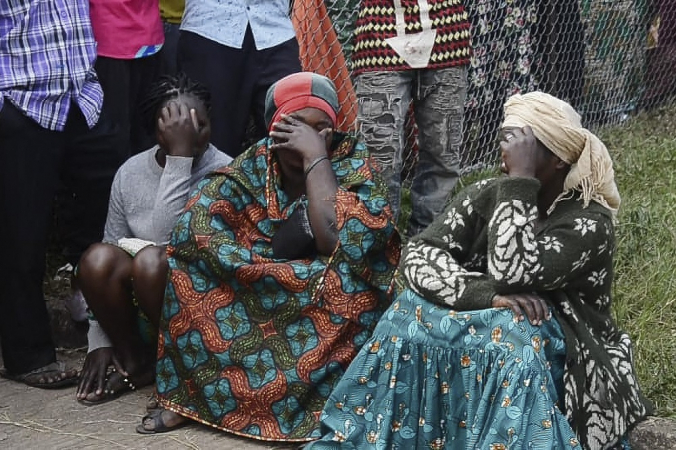 Pessoas sentadas no meio fio com a mão no rosto lamentam ataque em Uganda