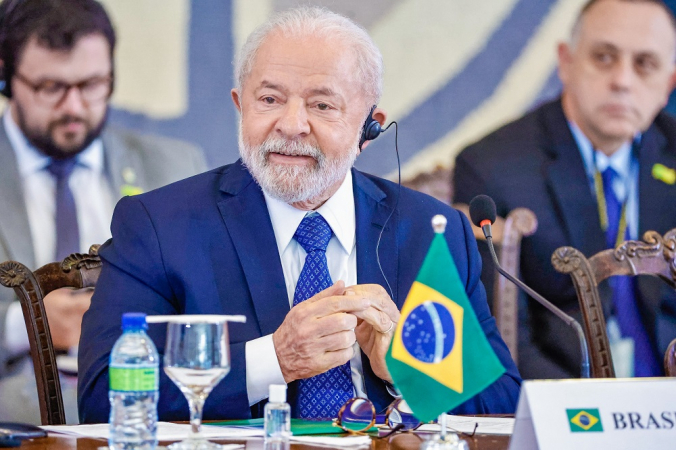 Lula sentado em lugar cmo água e uma bandeirinha do Brasil durante Abertura da Reunião de Presidentes dos países da América do Sul