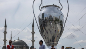 Pessoas caminham em torno de uma enorme maquete do troféu da UEFA Champions League tendo como pano de fundo a Mesquita Taksim