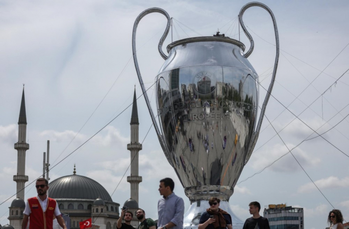 Pessoas caminham em torno de uma enorme maquete do troféu da UEFA Champions League tendo como pano de fundo a Mesquita Taksim