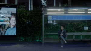 Cena de propaganda que mostra mulher sozinha em ponto de ônibus