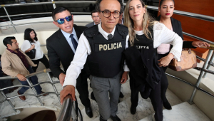 Christian Zurita e Andrea Gonzalez deixam uma coletiva de imprensa em um hotel, vestindo coletes da polícia