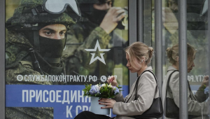 Uma mulher russa está sentada em um ponto de ônibus em frente a um cartaz anunciando o recrutamento militar mostrando soldados russos e a inscrição 'Junte-se ao seu. Trabalho de verdade.