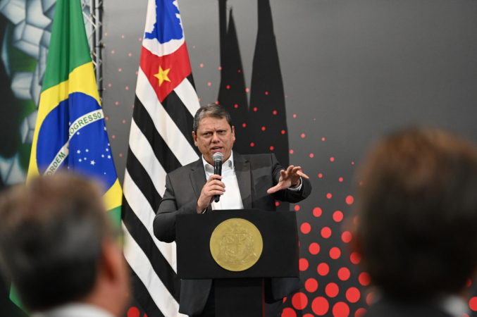 Tarcísio de Freitas discursa em púlpito e gesticula em frente às bandeiras de São Paulo e Santos