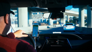 Visto de trás, Homem de boné dirige carro com auxílio de app de trajetos no celular