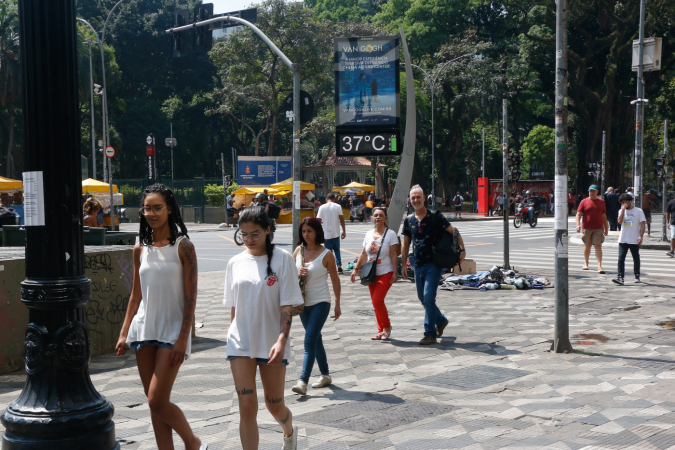 Pessoas andam na rua com termômetros marcando 37 graus