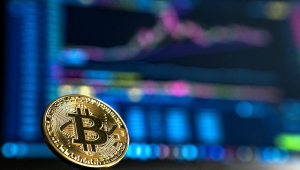 Bitcoin em freente a computador com gráficos de indicadores financeiros