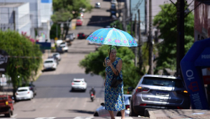 Idosa atravessa a rua com guarda-chuva para se proteger do sol