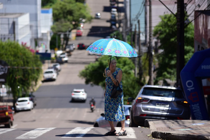 Idosa atravessa a rua com guarda-chuva para se proteger do sol