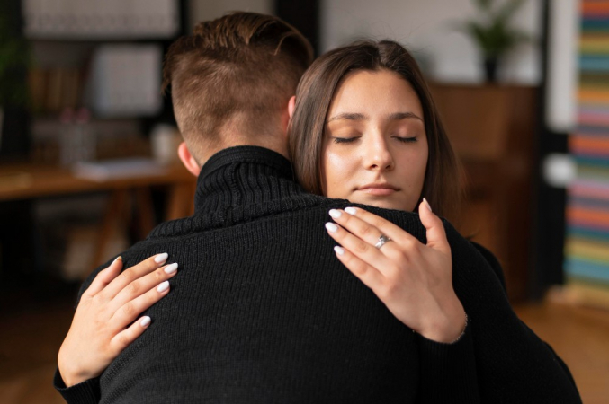 Homem e mulher se abraçam (ele de costas, ela de frente)