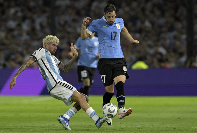 O meio-campista argentino Rodrigo De Paul (esq.) e o zagueiro uruguaio Matias Vina (dir.) brigam pela bola durante a partida de futebol das eliminatórias sul-americanas para a Copa