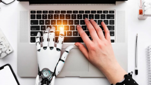 Mão robotizada e mão humana mexem em notebook