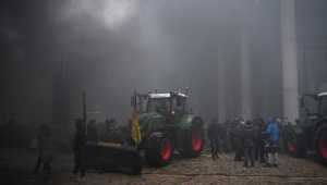 Agricultores reúnem-se perto de um trator enquanto a fumaça sobe durante um protesto em Bruxelas