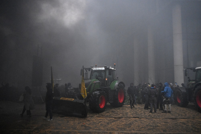 Agricultores reúnem-se perto de um trator enquanto a fumaça sobe durante um protesto em Bruxelas