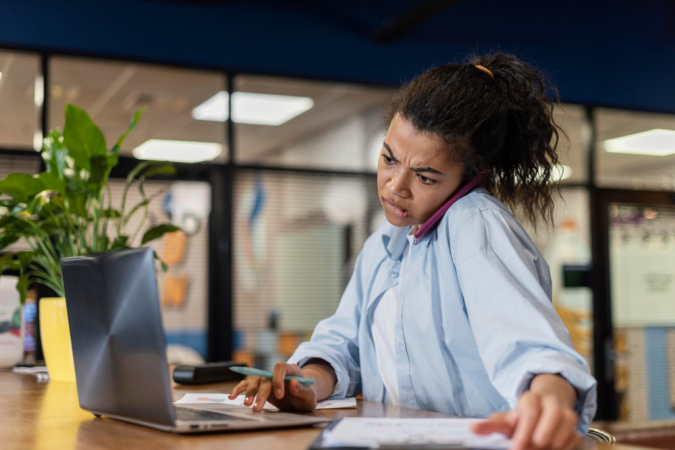 mulher estressada no escritório usando laptop e falando em smartphone