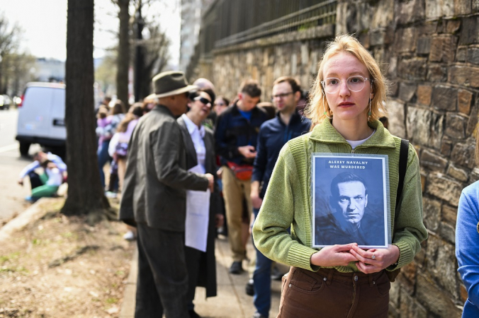 Mulher segura cartaz com o rosto de Navalny e a mensagem de que ele fo assassinado em fila para a votação na eleição russa em Washington