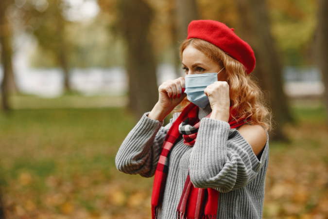 Mulher na floresta de outono. Pessoa com máscara. Tema Coronavirus. Senhora em um lenço vermelho.