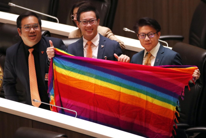 Os membros do Parlamento do Partido Move Forward (esquerda para a direita) Sorrapat Sriprach, Chutchawan Apirukmonkong e Prasit Puttamapadungsak seguram um tecido colorido do arco-íris para apoiar o LGBTQIA+ durante uma sessão legislativa realizada para reconhecer um projeto de lei de igualdade no casamento em Parlamento em Bangkok