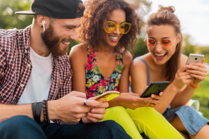 Amigos sorridentes sentados no parque usando smartphones,