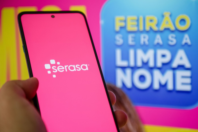 Celular com logo do Serasa ao lado de cartaz do Feirão Limpa Nome