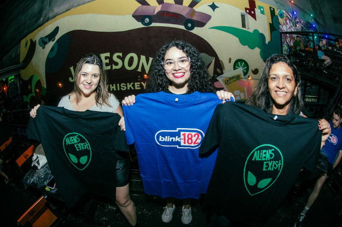 Fãs posam com as camisetas distribuídas no Baron Rock Bar, na Rua Augusta; Taynara (ao centro) não vai ao show