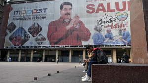 Pessoas caminham em frente a uma enorme faixa representando o presidente venezuelano Nicolás Maduro