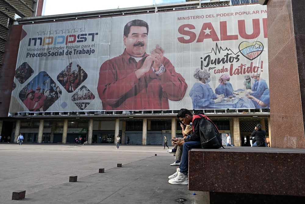 Pessoas caminham em frente a uma enorme faixa representando o presidente venezuelano Nicolás Maduro