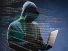Hacker de capuz com notebook na mão e diversos códigos sobrepndo a imagem