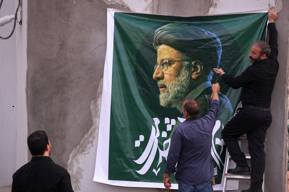 Homens penduram um enorme retrato do falecido presidente do Irã, Ebrahim Raisi, do lado de fora da embaixada iraniana em Bagdá
