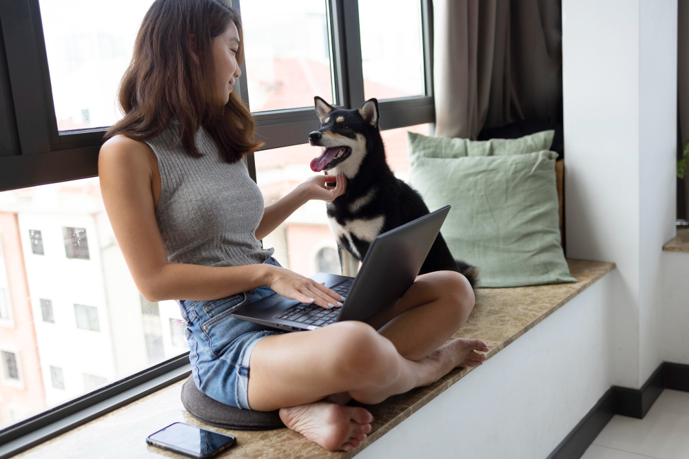 Jovem mulher se senta em bancada de apartamento com seu cachorro e o lap top no colo
