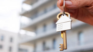 Mão segura chave de casa em frente a condomínio